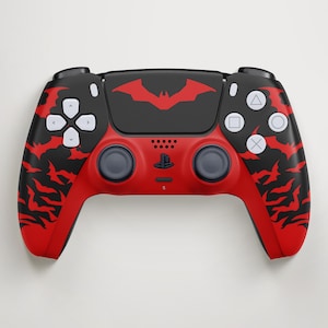 Peut inclure: Une manette de jeu vidéo sans fil avec un motif rouge et noir composé de silhouettes de chauves-souris répétées. Le pavé tactile central affiche un grand logo de chauve-souris rouge, avec des boutons blancs et des joysticks gris foncé.