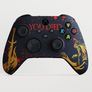 Könnte beinhalten: Schwarzer Xbox-Controller mit individuellem Design. Er zeigt den Text "YOU DIED" in Rot, ein goldenes Schwert und eine Kriegerfigur. Der Controller hat rote Spritzer und farbige Knöpfe.