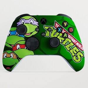Könnte beinhalten: Grüner Xbox-Controller mit den Teenage Mutant Ninja Turtles. Der Controller hat einen grünen Hintergrund mit den Gesichtern der Schildkröten und den Worten "Teenage Mutant Ninja Turtles" in einer kräftigen, stilisierten Schriftart. Die Tasten sind mit den Buchstaben A, B, X und Y beschriftet.