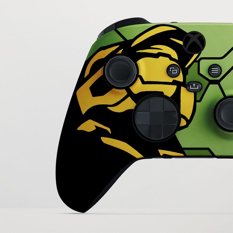 May include: An Xbox controller with a custom design. The controller has a black and yellow graphic on a green background. The buttons and joysticks are black. The Xbox logo is visible.