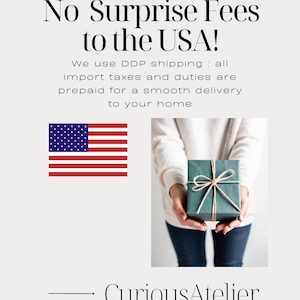 May include: Image features the text "No Surprise Fees to the USA!" and the American flag. A person holds a teal gift box tied with twine. The shop name "CuriousAtelier" is at the bottom.