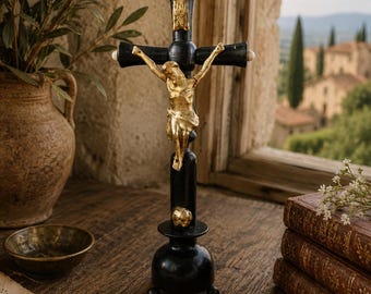 May include: A black standing crucifix featuring a gold-toned figure of Jesus attached to the center. The cross has a rounded base with three small feet, a gold-toned skull detail at the bottom of the vertical post, and a gold-toned INRI plaque.