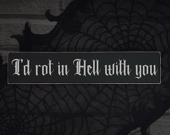 Może przedstawiać: Czarny prostokątny znak z napisem "I'd rot in Hell with you" w białych gotyckich literach. Znak jest umieszczony na ciemnym tle z motywem pajęczyny i fakturą przypominającą cegłę.