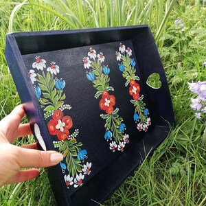 May include: A black wooden tray with a heart-shaped cutout handle. The tray is decorated with hand-painted floral designs in red, white, blue, and green.
