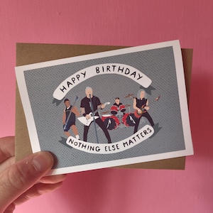 May include: A rectangular greeting card with a gray background featuring a cartoon illustration of a four-piece rock band. The text "HAPPY BIRTHDAY" is printed on a white banner above the band, and "NOTHING ELSE MATTERS" is on a banner below.