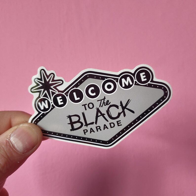 K&ouml;nnte beinhalten: Ein schwarz-wei&szlig;er Aufkleber mit dem Text "WELCOME TO THE BLACK PARADE". Das Design ist im Retro-Stil gehalten, mit einem Stern-Burst-Grafik. Der Aufkleber hat einen wei&szlig;en Rand und befindet sich auf einem rosa Hintergrund.