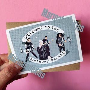 Könnte beinhalten: Eine rechteckige Grußkarte mit hellblau gepunktetem Hintergrund zeigt eine Comic-Illustration einer vierköpfigen Rockband. Der Text "WELCOME TO THE BIRTHDAY PARADE" steht auf weißen Bannern. Die Bandmitglieder tragen schwarze Uniformen.