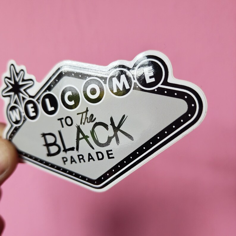 K&ouml;nnte beinhalten: Ein Aufkleber in Form eines Retro-Schildes mit den Worten "WELCOME TO The BLACK PARADE" in Schwarz und Wei&szlig;. Das Schild hat einen schwarzen Rand mit wei&szlig;en Punkten und ein Sternmuster auf der linken Seite.