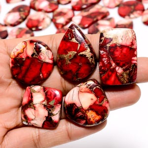 May include: Six red, white, and gold gemstone cabochons with a marbled pattern. The cabochons are various shapes and sizes.
