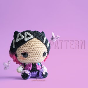 Pode incluir: Uma boneca amigurumi de crochê com cabelo preto, luzes rosa e uma faixa de cabeça branca e cinza. A boneca está vestindo uma roupa roxa e rosa e está sentada em um fundo rosa. A palavra "PATTERN" é visível no fundo.