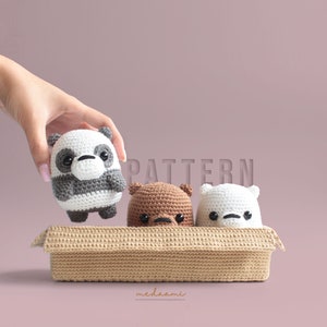 Op de afbeelding: Drie gehaakte knuffels in een bruine rieten mand. De beren zijn een panda, een bruine beer en een ijsbeer. De panda wordt vastgehouden door een hand.