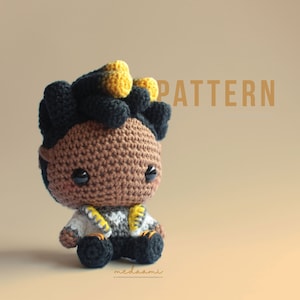 Pode incluir: Padrão de crochê para uma boneca amigurumi marrom e preta com cabelo amarelo. A boneca está sentada e usa uma jaqueta branca e cinza. O texto "PATTERN" está escrito em letras douradas acima da boneca.