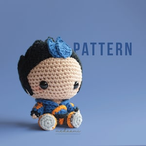 May include: A crocheted amigurumi toy of a character with blue hair, a blue and orange shirt, and gray pants. The toy is sitting on a blue background. The word "PATTERN" is written in white letters on the background.