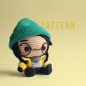 May include: Crochet amigurumi pattern for a small person wearing a teal beanie, yellow jacket, and glasses. The pattern is called "PATTERN".