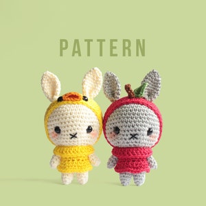 Puede incluir: Dos peluches de conejo tejidos a crochet vestidos con disfraces. Un conejo lleva un disfraz de pollito amarillo y el otro lleva un disfraz de manzana roja. Los conejos tienen ojos negros y una nariz negra.