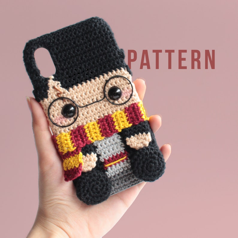 Peut inclure: Une coque de t&eacute;l&eacute;phone crochet&eacute;e repr&eacute;sentant un personnage de dessin anim&eacute; avec des cheveux noirs, des lunettes rondes, une &eacute;charpe rouge et jaune et une tenue grise et noire. La coque porte l'inscription "PATTERN" sur le fond.
