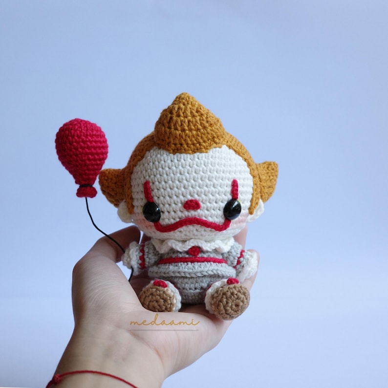 Peut inclure: Un jouet en crochet repr&eacute;sentant le clown Pennywise, personnage du film &Ccedil;a. Le jouet tient un ballon rouge et a un visage blanc avec des l&egrave;vres rouges et des yeux noirs. Le jouet porte une tenue grise et rouge.