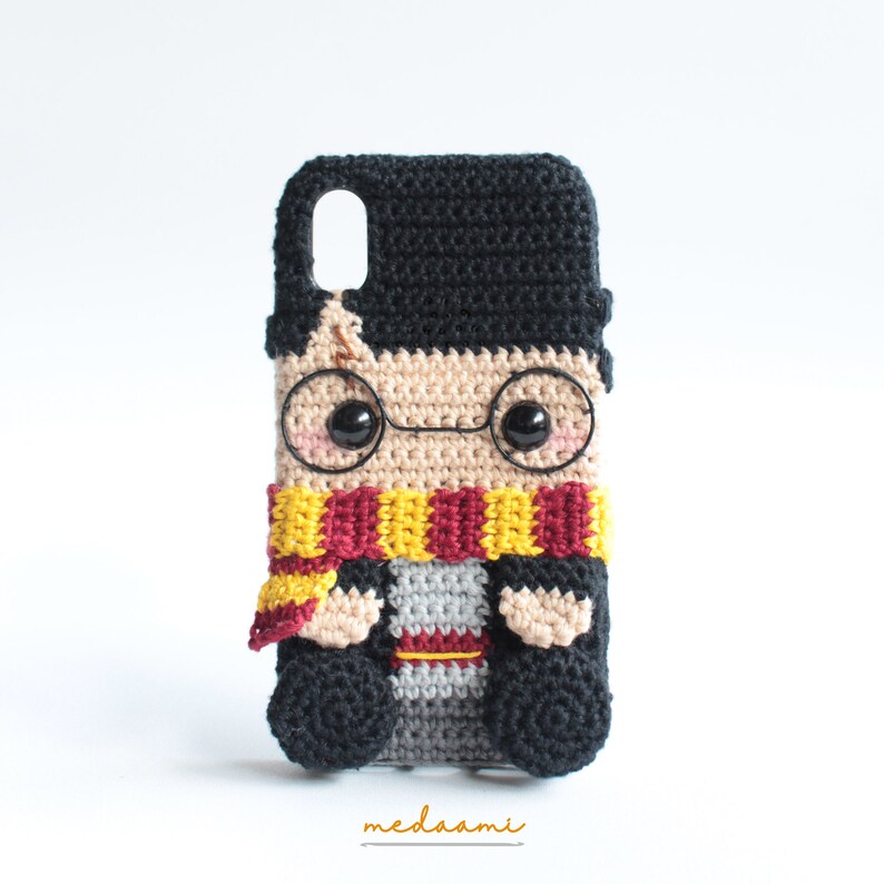 Peut inclure: Une coque de t&eacute;l&eacute;phone en crochet repr&eacute;sentant un personnage de dessin anim&eacute; de Harry Potter avec des cheveux noirs, des lunettes rondes, une &eacute;charpe rouge et jaune et une robe grise et rouge.