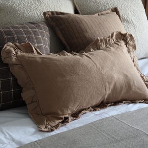 May include: A close-up of a bed with a variety of pillows. The pillows are made from different fabrics and have different textures. The pillows are arranged in a way that is both stylish and comfortable. The bed is made from a white fabric and has a white blanket on top of it.