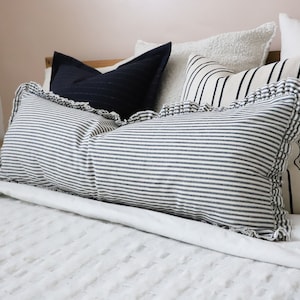 May include: A white bed with a white duvet cover and several pillows. The pillows are striped in black and white and have a ruffled edge. There is a dark blue pillow in the background.