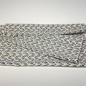 Könnte beinhalten: Gefalteter Stoff mit cremefarbenem Hintergrund und einem sich wiederholenden Muster aus dunkelblauen Blattformen. Der Stoff ist über sich selbst gefaltet, wodurch ein geschichteter Effekt entsteht. Das Material scheint eine Naturfaser zu sein.