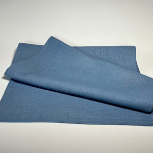 Könnte beinhalten: Ein gefaltetes blaues Leinen-Platzset. Das Platzset ist aus natürlichem Stoff gefertigt und hat eine dezente Textur.