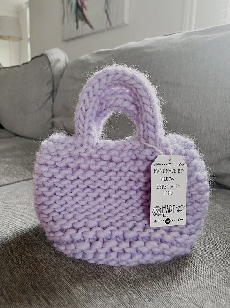 K&ouml;nnte beinhalten: Eine lavendelfarbene Stricktasche mit einem wei&szlig;en Etikett, auf dem "Handmade by HeeJu Especially for Made with love" steht.