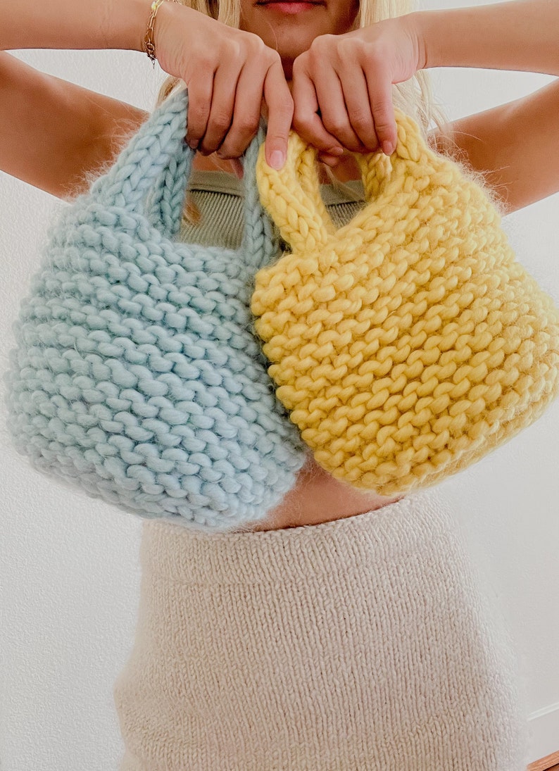 K&ouml;nnte beinhalten: Zwei gestrickte Einkaufstaschen, eine hellblau und eine gelb, die von den H&auml;nden einer Person gehalten werden.