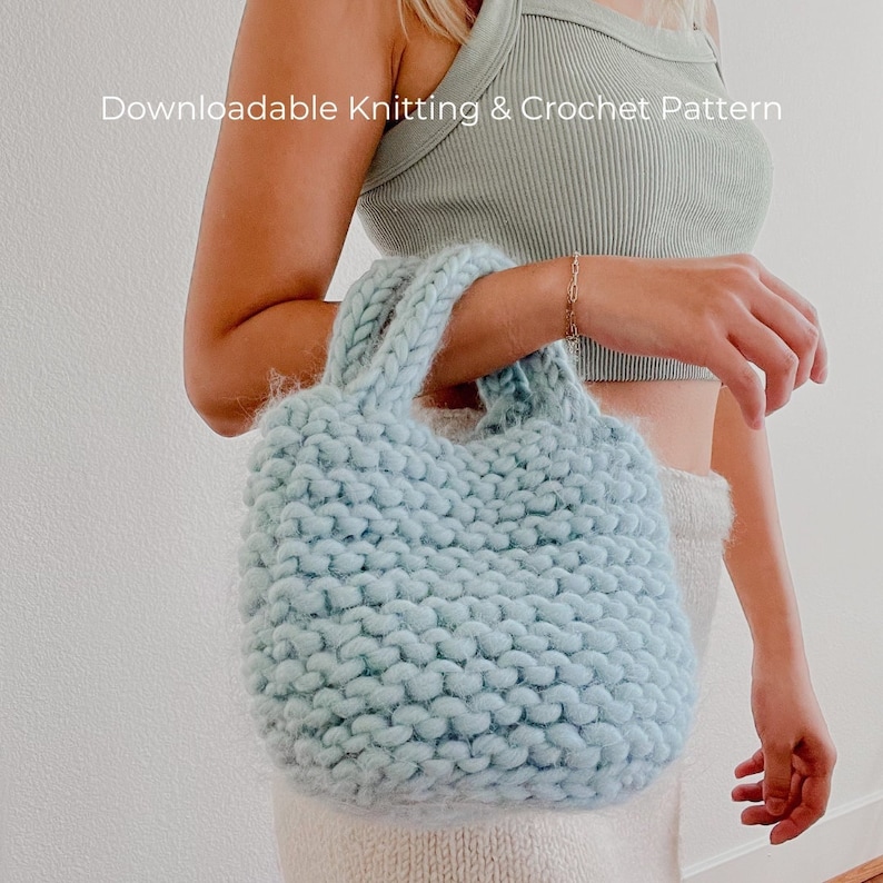 K&ouml;nnte beinhalten: Eine hellblaue Stricktasche mit dickem Garn und einer grobmaschigen Textur. Die Tasche hat zwei Henkel und wird von einer Person gehalten.