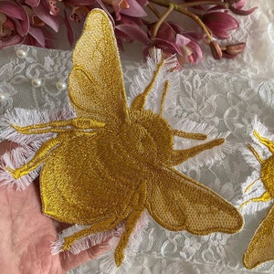 Peut inclure: Patch brodé d'abeille dorée avec des bords effilochés blancs. L'abeille est détaillée avec un corps et des ailes texturés.
