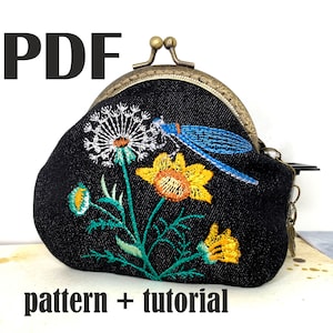 May include: A black denim coin purse with an embroidered floral design featuring a dandelion, a yellow flower, and a blue dragonfly. The purse has a brass clasp and a chain.