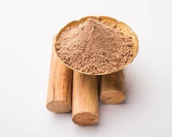 May include: A golden bowl filled with brown powder sits atop three cylindrical pieces of light brown wood. The wood pieces are arranged vertically, with the bowl resting on top. The background is plain white.