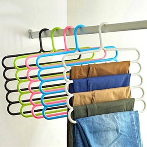 Puede incluir: Una percha de ropa de varias capas en negro, verde, rosa, azul y blanco, que sostiene varios pares de pantalones. Las perchas están diseñadas para ahorrar espacio y organizar la ropa en un armario.