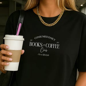 Può includere: T-shirt nero con la scritta bianca "CONSUMED DAILY BOOKS & COFFEE Club I'm a lifestyle". La persona indossa una collana a catena dorata e tiene in mano una tazza di caffè bianca con un manicotto marrone.