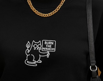 May include: A black crewneck sweatshirt featuring a white embroidered graphic of a cat wearing glasses, holding a lit match, and carrying a sign that reads BURN THE PATRIARCHY. The sweatshirt has long sleeves and a ribbed neckline.