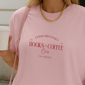 Könnte beinhalten: Ein hellrosa T-Shirt mit kurzen Ärmeln und dunkelrotem Text, der CONSUMED DAILY EST 2023 BOOKS AND COFFEE Club i'ts a lifestyle lautet. Das T-Shirt wird mit hellrosa-weiß gestreiften Shorts und einer passenden rosa Umhängetasche kombiniert.