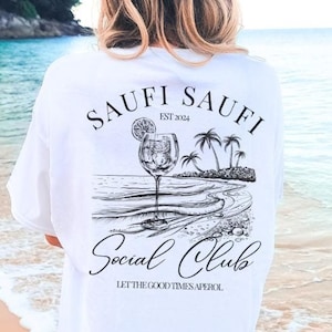 May include: White t-shirt with a black graphic on the back. The graphic includes the text "SAUFI SAUFI EST 2024" above a drawing of a cocktail, palm trees, and the text "Social Club, Let the good times Aperol."