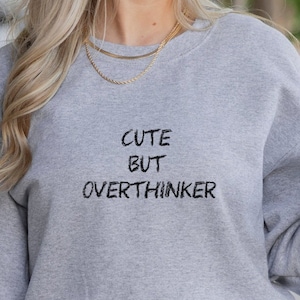May include: A grey sweatshirt with the text "Cute but Overthinker" printed on the front.
