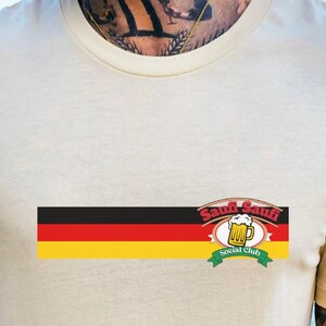 May include: Cream-colored t-shirt featuring a German flag design with the words "Sauf-Sauf Social Club" and a beer mug graphic. The shirt is short-sleeved and made of a soft material.
