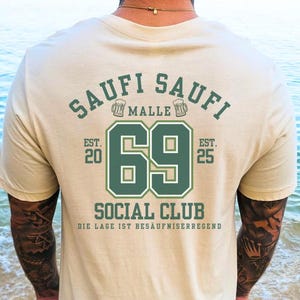 May include: A beige t-shirt with a green graphic print that says "Saufi Saufi Malle Est. 20 69 Est. 25 Social Club Die Lage Ist Besaufniserregend"