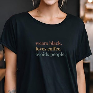Könnte beinhalten: Ein schwarzes T-Shirt mit dem Text "wears black. loves coffee. avoids people." in bunten Buchstaben.