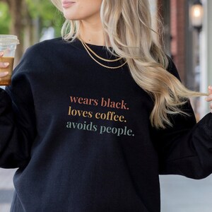 Könnte beinhalten: Ein schwarzer Pullover mit dem Aufdruck "wears black. loves coffee. avoids people." auf der Vorderseite.