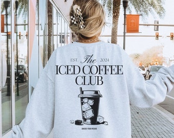 Op de afbeelding: Lichtgrijze sweatshirt met de tekst "The Iced Coffee Club" en een afbeelding van een ijskoffie. De sweatshirt heeft lange mouwen en een ronde hals. De tekst "Est. 2024" staat boven de clubnaam.