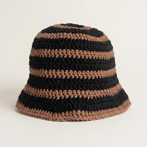 Könnte beinhalten: Ein gehäkelter Bucket Hat mit schwarzen und braunen Streifen. Der Hut hat abwechselnd horizontale Streifen in Schwarz und Braun. Der Rand ist leicht ausgestellt und der Hut ist aus weichem, strukturiertem Garn gefertigt.
