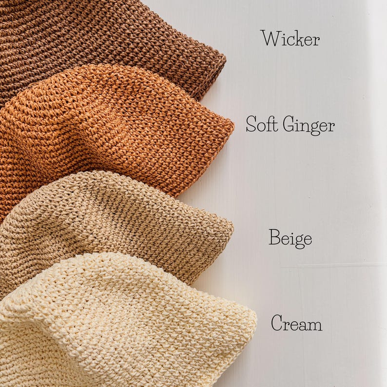 May include: Four crocheted bucket hats in shades of brown, orange, beige, and cream. The hats are displayed in a row, with the names "Wicker", "Soft Ginger", "Beige", and "Cream" written next to each hat. The hats have a textured appearance.