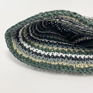 Puede incluir: Primer plano de un sombrero tejido a mano. El sombrero presenta una mezcla de hilos verdes, blancos, grises y negros, creando un patr&oacute;n de rayas. La textura del sombrero es visible, mostrando la artesan&iacute;a. El sombrero es probablemente para protecci&oacute;n solar o moda.