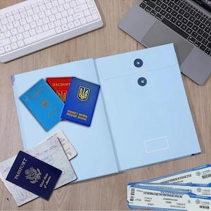 May include: A light blue document folder with a string-and-button closure, three Ukrainian passports in blue and red, a dark blue United States passport, and two printed airline boarding passes arranged on a wooden surface.