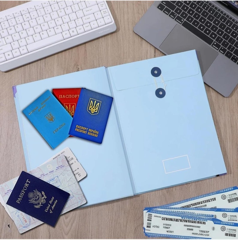 May include: A light blue document folder with a string-and-button closure, three Ukrainian passports in blue and red, a dark blue United States passport, and two printed airline boarding passes arranged on a wooden surface.
