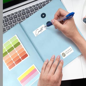 May include: A light blue organiser folder with two dark circular snap closures. The folder features a white label with the word Credit written in black ink, a second label reading gift cards & credit cards, and two sheets of colourful adhesive labels.