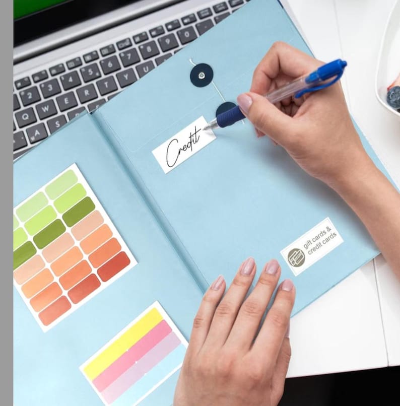 May include: A light blue organiser folder with two dark circular snap closures. The folder features a white label with the word Credit written in black ink, a second label reading gift cards & credit cards, and two sheets of colourful adhesive labels.